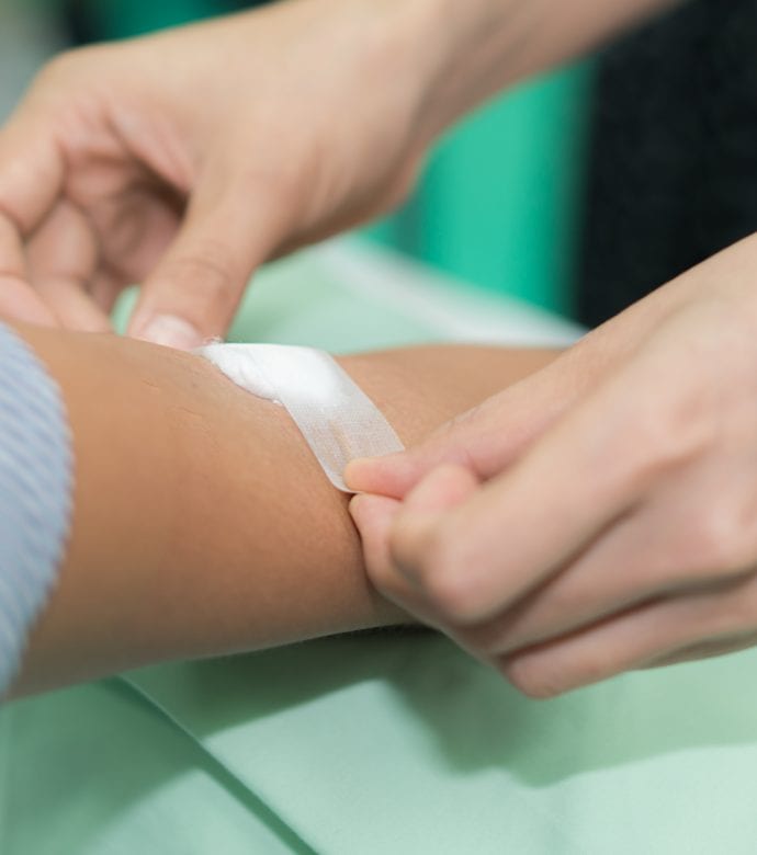 Nurse applying bandage on patient's hand after blood test in hospital.