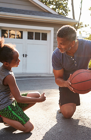 Father Teaching Son How To Play Basketball On Driveway At Home