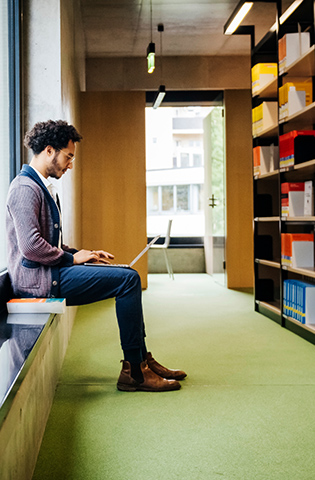 Man Sitting By Large Window Working In Library